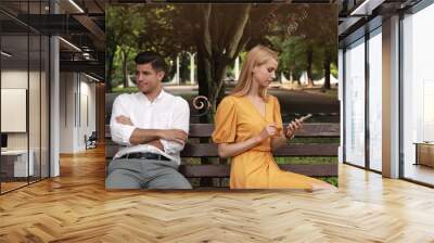 Young woman with smartphone ignoring her boyfriend in park. Boring date Wall mural