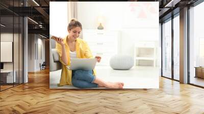 Young woman with smartphone using laptop at home Wall mural