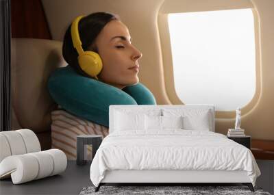 Young woman with travel pillow resting while listening to music in airplane during flight Wall mural