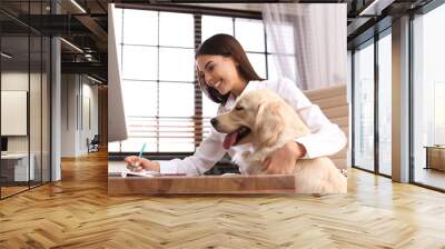 Young woman working at home office and stroking her Golden Retriever dog Wall mural