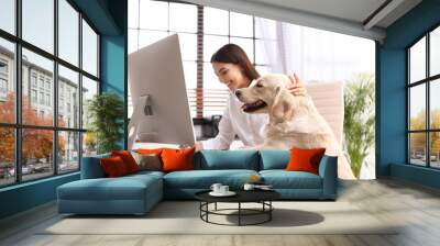 Young woman working at home office and stroking her Golden Retriever dog Wall mural