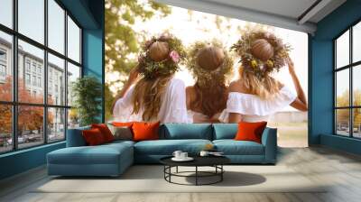 Young women wearing wreaths made of beautiful flowers outdoors on sunny day, back view Wall mural