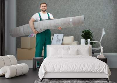 Young worker carrying rolled carpet in room. Moving service Wall mural