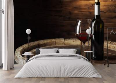 Bottle and glass of red wine on wooden barrel shot with dark wooden background Wall mural