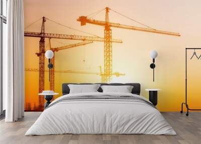 Silhouetted construction cranes against a vibrant sunset in an urban landscape Wall mural