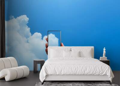 Smart phone  in hand on blue sky background Wall mural