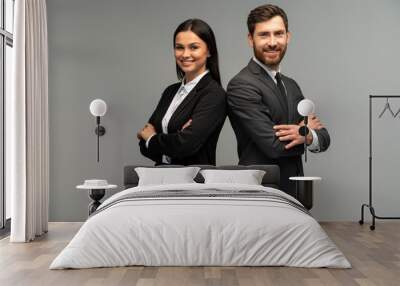 Concept of partnership in business. Young man and woman standing back-to-back with crossed hands against grey background Wall mural