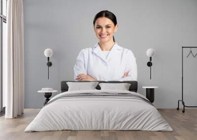 Photo of young happy woman professional wearing suit smiling friendly while posing arms crossed to the camera isolated on grey color background Wall mural