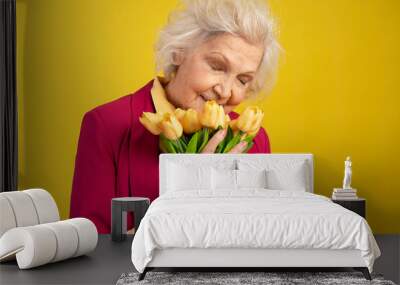 Senior caucasian woman with closed eyes sniffing bouquet of yellow tulips Wall mural