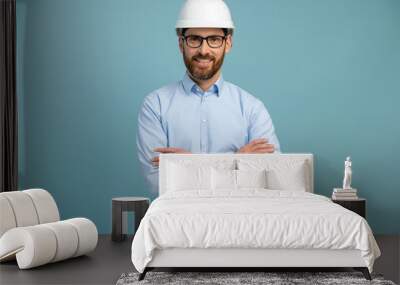 Young architect man with happy face in builder safety helmet smiling while looking at the camera and posing arms crossed over isolated background Wall mural