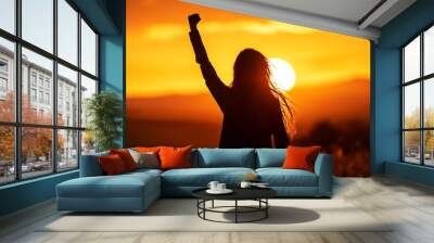 Silhouette of a woman raising her fist in the air during a sunset. Wall mural