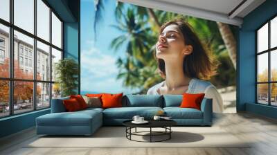 Beautiful young woman enjoying the fresh beach air against a backdrop of palm trees. Beautiful woman in white shirt lounging and taking pleasure in her tropical coast vacation. Idea for a travel vacat Wall mural