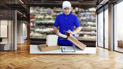 Food delivery service or shopping order food online. Man putting in takeout food container into paper bag and packaging on supermarket background. Wall mural