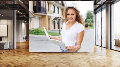 Beautiful woman traveler holding location map in hands in a city Wall mural