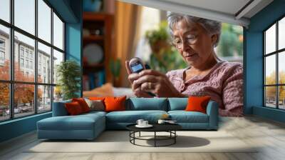 A senior woman is comfortably seated while checking her glucometer, symbolizing both the routine nature of diabetes management and the comfort of conducting such important tasks at home. Wall mural