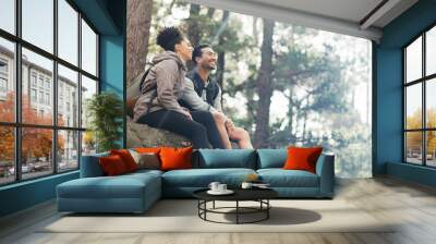 Nature, hiking and a couple relax on adventure trail in forest and sitting on a rock. Health, happy man and woman pointing at natural landscape while relaxing in woods with trees, fitness and freedom Wall mural