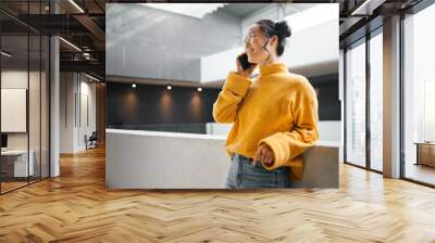 Phone call, communication and mockup with an asian woman talking while standing in a hallway. Mobile, networking and conversation with an attractive young female speaking on her smartphone indoor Wall mural