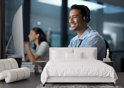 Courtesy and professionalism pays off. Shot of a young man using a headset and computer in a modern office. Wall mural