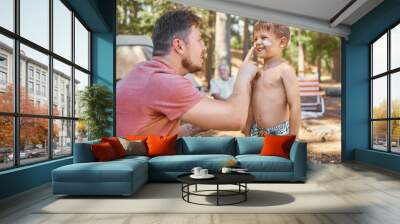 Dont forget your sunscreen. Cropped shot of a handsome young man putting sunblock on his adorable little son while camping in the woods. Wall mural