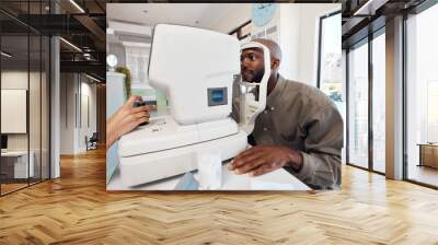 Eye test, exam or screening with a young man at the optometrist using an automated refractor. Patient testing his vision and eyesight with an optician for prescription glasses or contact lenses Wall mural