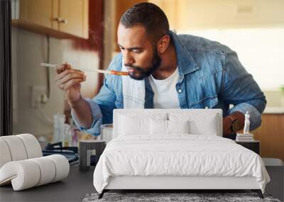 I keep surprising myself in the kitchen. Shot of a man using a wooden spoon to taste his food while cooking. Wall mural