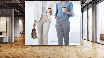 Lets go run this day. Shot of two businesswomen carrying coffees while walking through an office. Wall mural