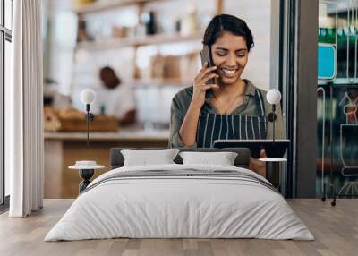 The wireless barista. Shot of a young woman using a digital tablet and smartphone while working in cafe. Wall mural