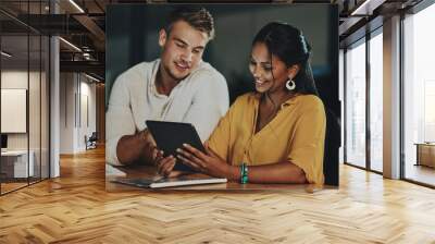 The world online will enable them to beat the deadline. Shot of two businesspeople using a digital tablet together in an office at night. Wall mural