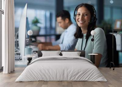 We work to make you happy. Portrait of a young woman using a headset and computer in a modern office. Wall mural