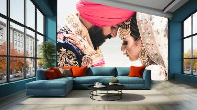 Sikh bride and groom wearing bright traditional clothing on clear sandy beach beneath sunny blue skies Wall mural