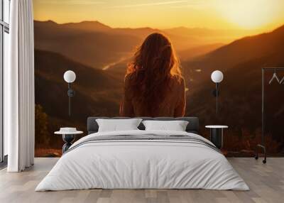 a woman sitting on top of a mountain at sunset Wall mural