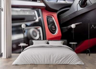 Close-up, isolated image of an engine Start Stop button seen on the dashboard of a german manufactured sports car, also showing its part red leather. Wall mural