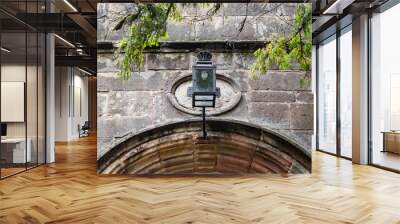 Wrought Iron decorative lantern seen at the entrance to an old, medieval building. A new style, energy efficient bulb is seen within the lantern itself. Wall mural