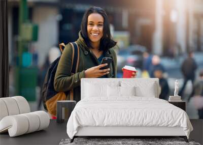 Beautiful latin student woman drinking coffee outdoors on city street and texting on mobile phone. Beautiful young student girl with a bag smiling outdoors. Wall mural