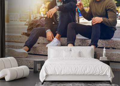 lifestyle photo of two male friends sitting on the steps in city street and talking wearing casual s Wall mural