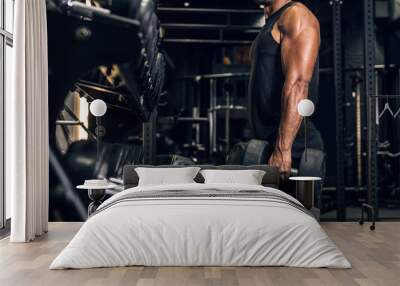 Strong muscular man holds dumbbells and doing a  workout in the gym Wall mural