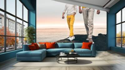 Two male models wearing fashionable spring summer outfit with colorful pants, t-shirt, sweater and shoes walking outdoors on the rock ocean beach Wall mural