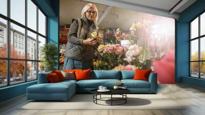 Woman - gardener in the flower shop make bouquet for a holiday. Family flower's business. Lifestyle flower shop. Beautiful flower composition. Love to flower's.Sunlight.  Wall mural