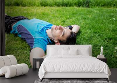 Sport fitness man relaxing listening to music after training outdoor in a city park . Young male athlete resting relaxing lying on grass after running and training exercise outside in summer. Wall mural