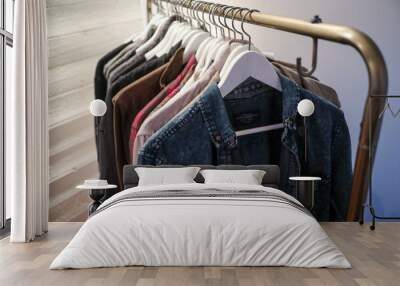 Clothes in the forms of sweaters and shirts of different textile fabrics and colors are haning on hangers on a clothing rack in a bedroom Wall mural