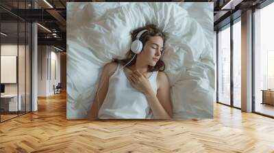 A woman is sleeping with headphones on. She is wearing a white tank top. Concept of relaxation and tranquility Wall mural