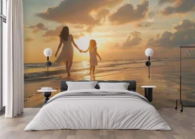 Mother and her daughter enjoying walk along beach at sunset. The woman is holding the child's hand. Wall mural