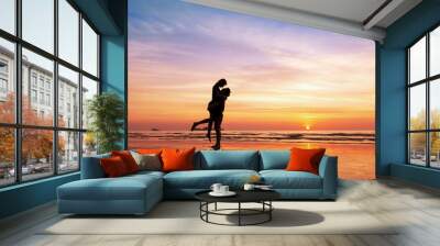 Couple kissing on the beach with beautiful sunset in background Wall mural