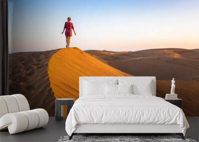 Girl walking on sand dunes in arid desert at sunset and wearing dress, scenic landscape of Sahara or Middle East Wall mural