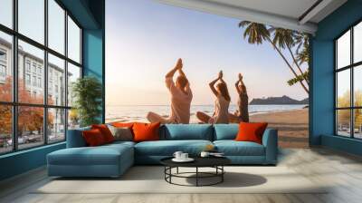 People practicing yoga on the beach, wellbeing, warm tropical landscape Wall mural