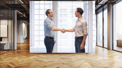 two colleagues dressed casually shaking hands in modern office interior Wall mural