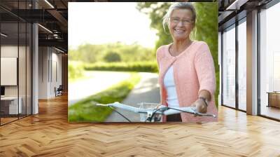 She enjoys healthy outdoor activities - Cycling. Smiling senior woman standing on a country lane with her bicycle. Wall mural