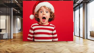 adorable surprised kid wearing a Santa Claus hat and striped sweater on a red background Wall mural