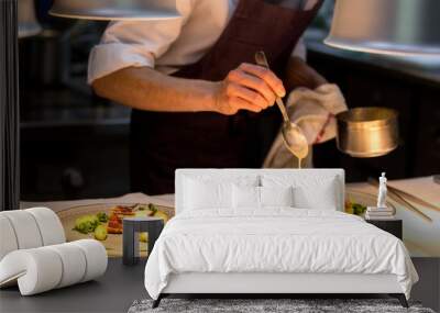 Chef preparing a plate made of meat and vegetables. The chef is pouring sauce on two plates. Wall mural