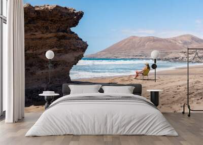 Side view of young woman Sitting on a chair in a beach looking the sea in Fuerteventura, Canary Island Wall mural